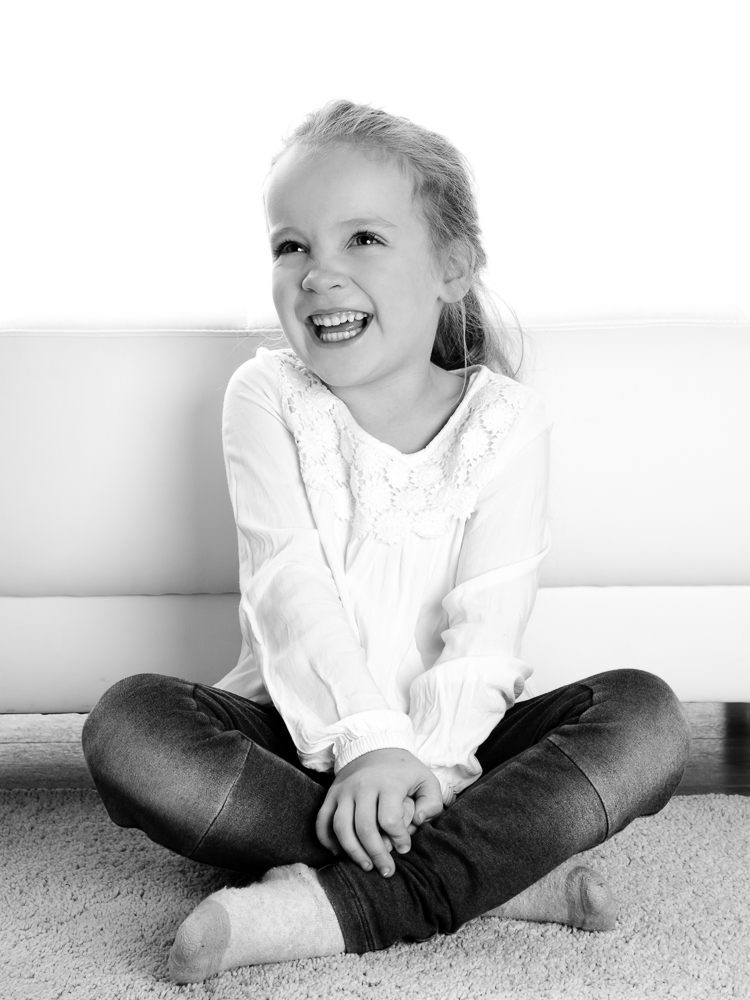 Kinderfoto in schwarz-weiß, lachendes Mädchen im Schneidersitz